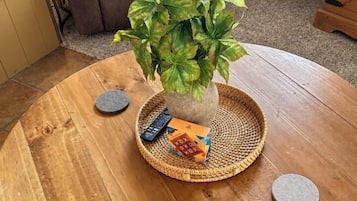 Ein runder Holztisch mit einer gewebten Tischmatte, einem Blumentopf, einer Fernbedienung und einem kleinen Dekoelement.