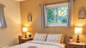 Ein Schlafzimmer mit einem Bett, zwei Nachttischen, einem fenster mit Vorhängen, einem Wandbild und einem Teppich.