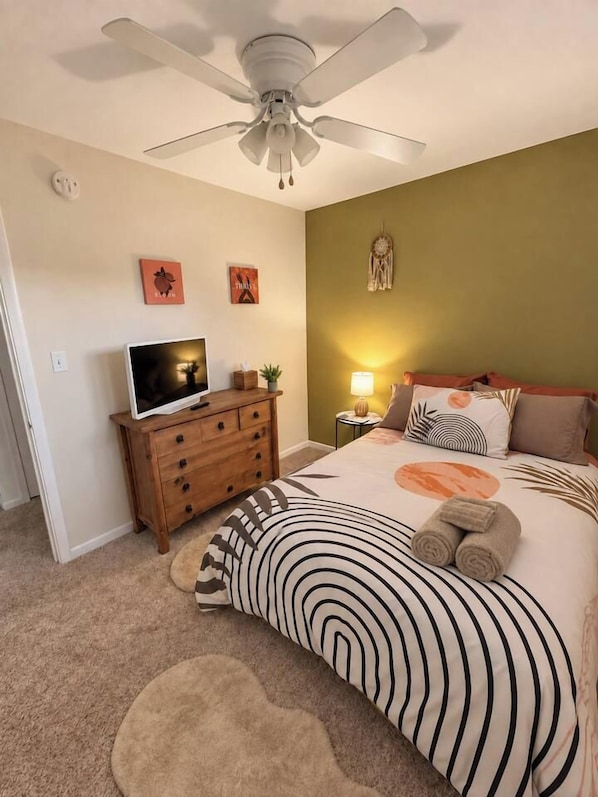 A bedroom with a bed, a ceiling fan, a TV on a wooden dresser, and wall decorations. - 3BR Chadron home near CSC + fire pit (Chadron)