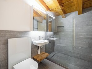 Ein modernes Badezimmer mit Holzboden, einem großen Spiegel, zwei Waschbecken und einer Duschkabine.