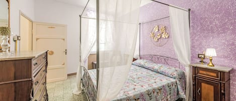 A four-poster bed with a floral bedspread, a nightstand with a lamp, a dresser, and a wall with a circular floral decoration.