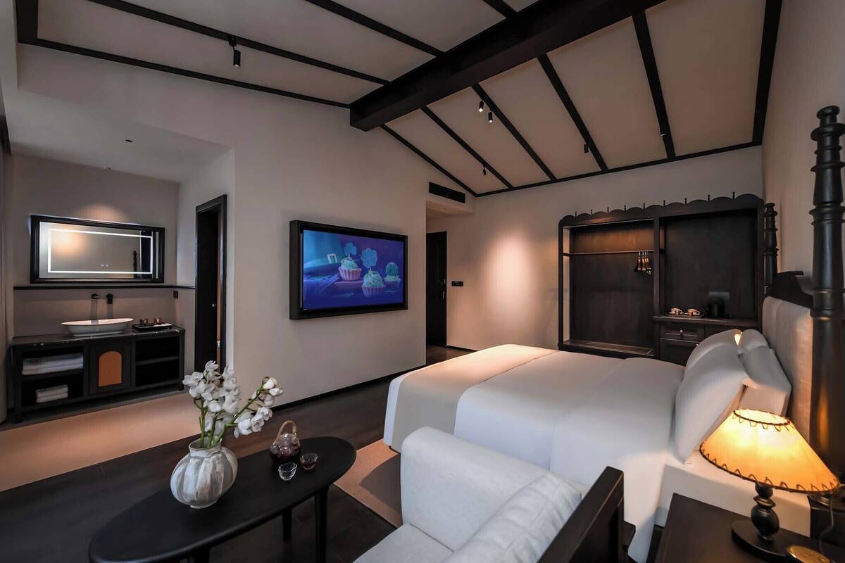 A modern hotel room with a large bed, a TV, a vanity with a mirror, and a small table with a vase of flowers.