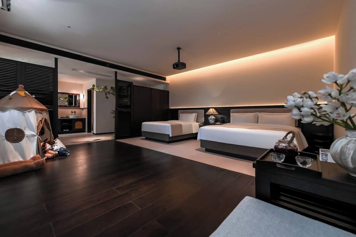 A modern hotel room with a large bed, bedside tables, a small seating area, and a view of the adjacent bathroom.