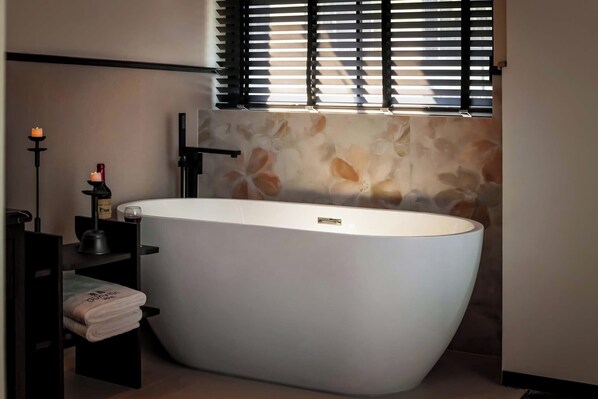 A modern bathroom with a freestanding bathtub, a towel rack, and a window with blinds. - Guanyin Shibaju Resort Hotel (Chongqing)