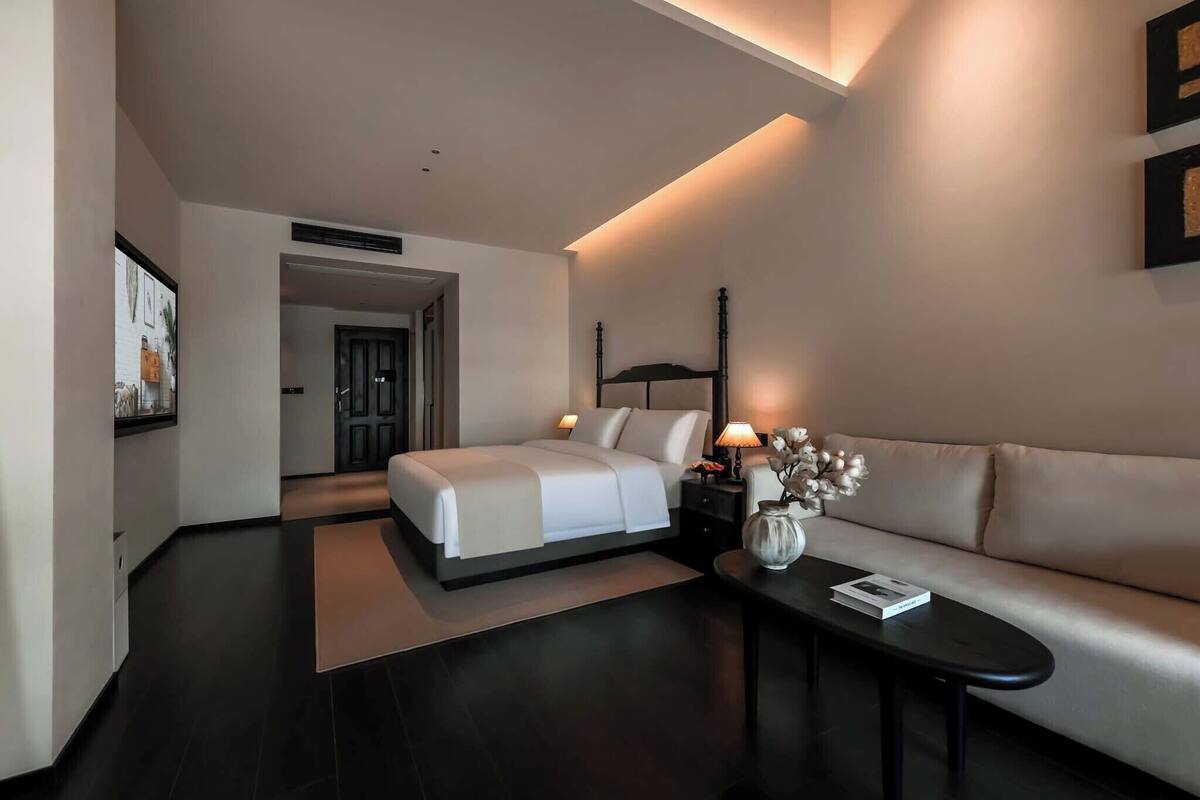 A modern hotel room with a bed, a sofa, a coffee table, and a vase with flowers.