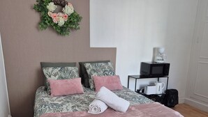 Een slaapkamer met een bed, kussens, een deken, een koffiezetapparaat en een magnetron op een bijzettafeltje.