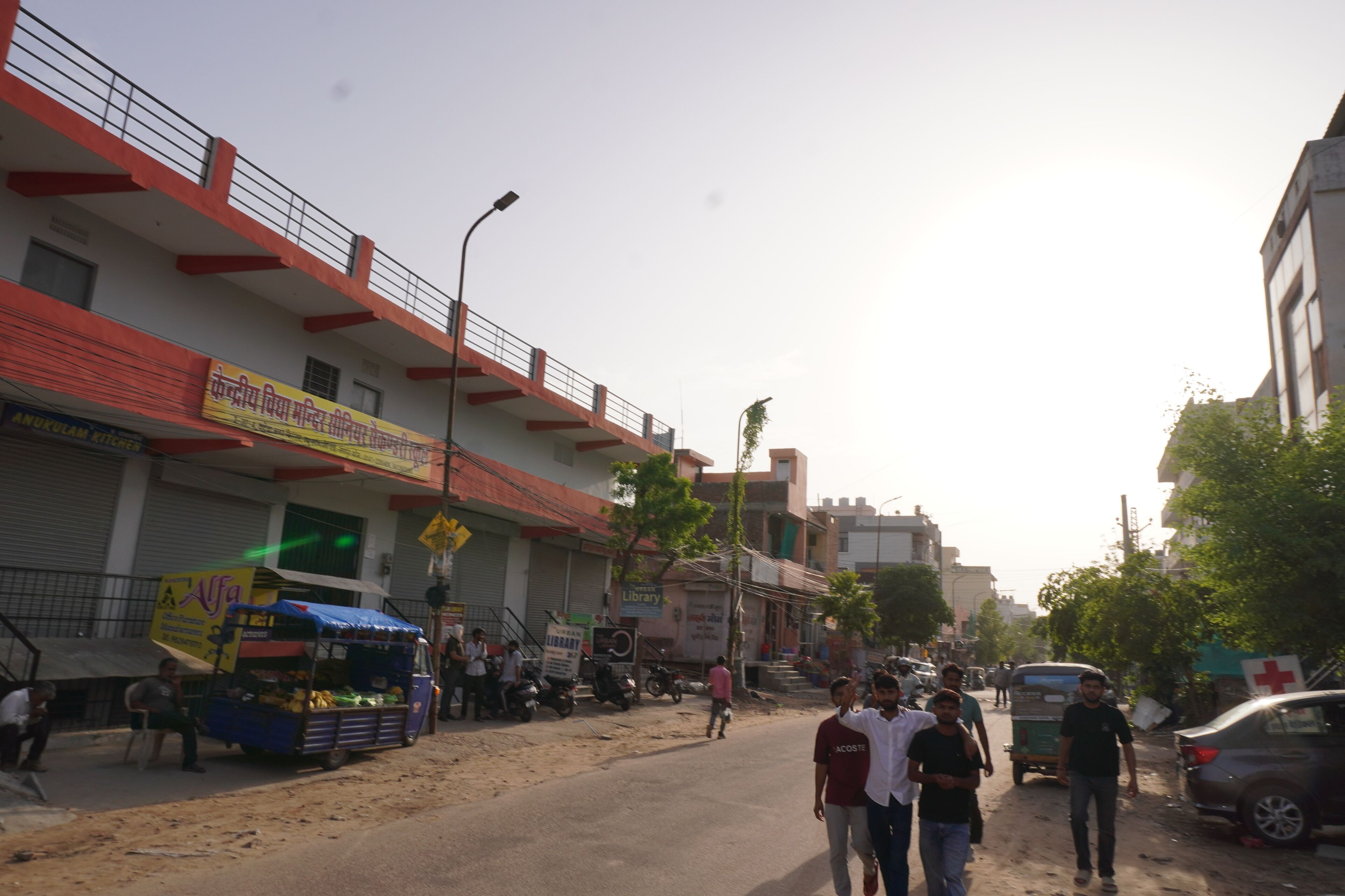 A street with buildings, a blue auto-rickshaw, and pedestrians.