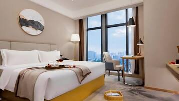 A hotel room with a large bed, a desk, a chair, a view of the city, and a painting on the wall.