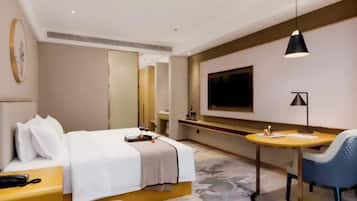 A modern hotel room with a bed, bedside table, TV, and a small round table with a chair.