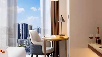 A hotel room with a bed, a chair, a table with a lamp, a window with a view of buildings, and a minibar with glasses.