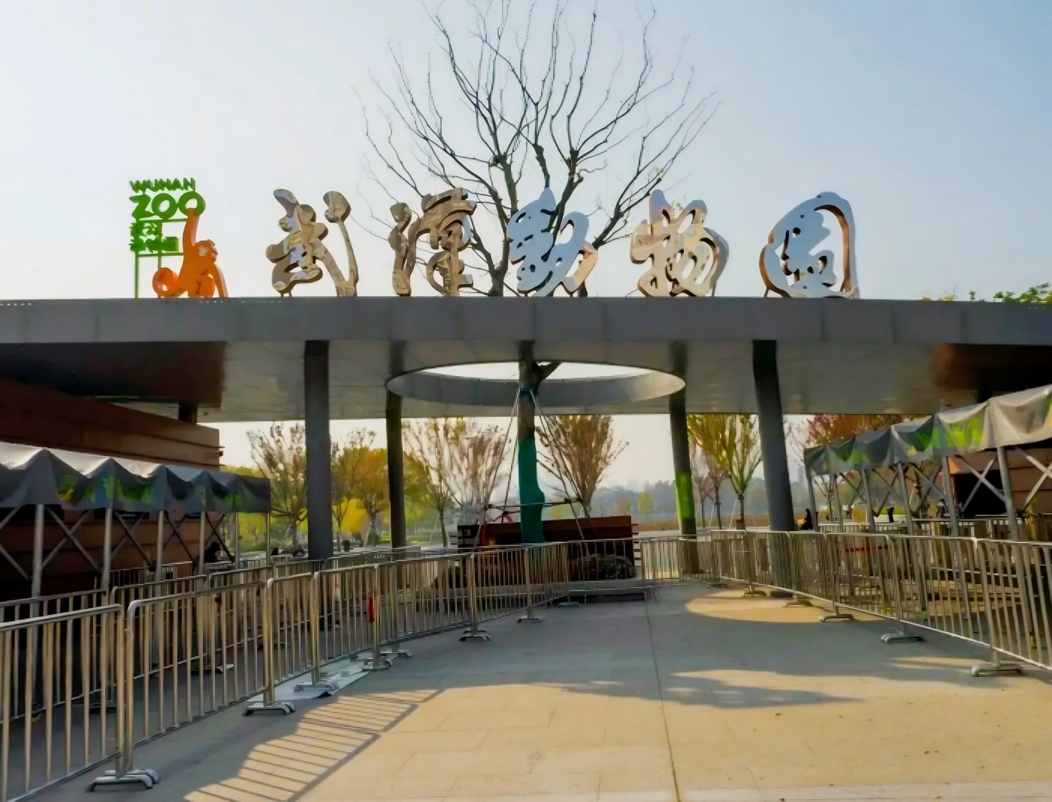 A zoo entrance with a sign, metal barriers, and a covered walkway.