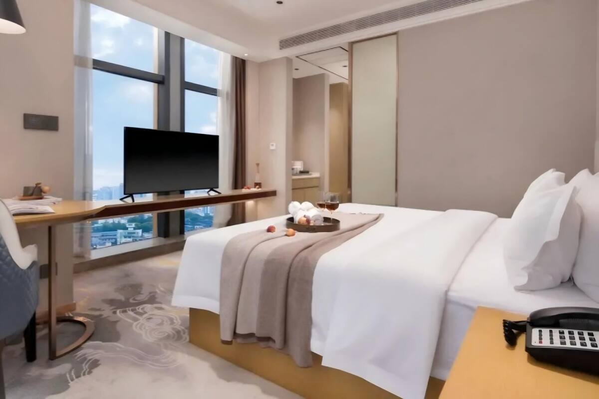 A hotel room with a bed, a desk with a TV, a phone, and a city view.