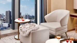 Ein modernes Wohnzimmer mit Blick auf die Stadt, ein runder Tisch mit einem Getränk, ein bequemer Sessel und ein kleiner Hocker.