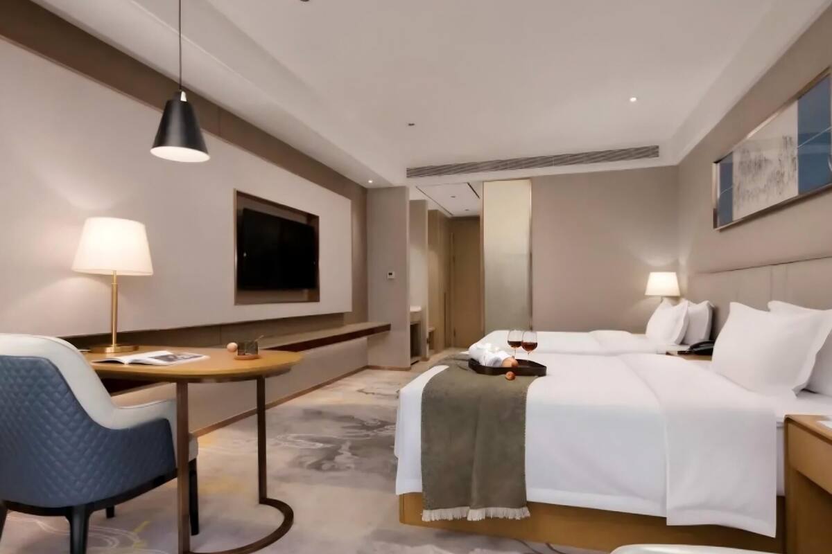 A hotel room with a bed, bedside table, lamp, chair, and a TV mounted on the wall.