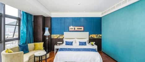 A modern bedroom with a large bed, a sofa, a small table, and a window with curtains.