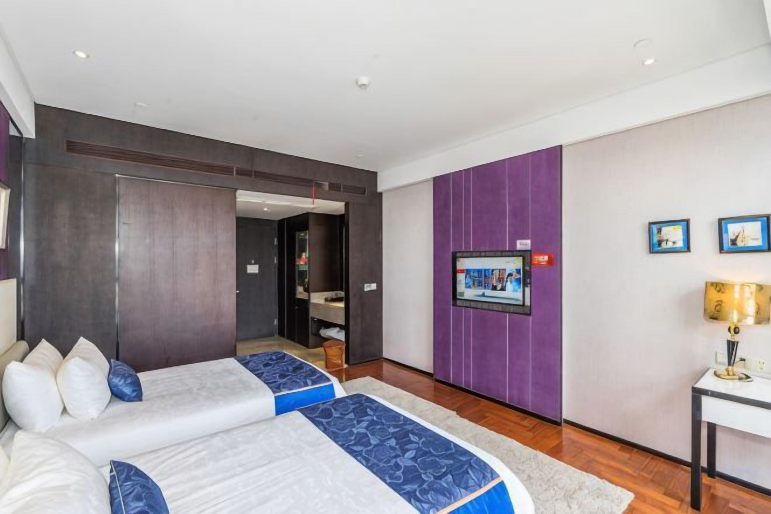 A hotel room with two beds, a television, a desk, and a bathroom.