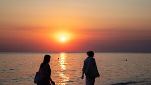 Zwei Personen spazieren am Strand entlang bei Sonnenuntergang.