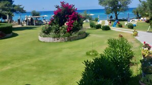 Ein gepflegter Garten mit Rasen, einem Blumengarten mit rosa Blüten und freiem Blick auf das Meer im Hintergrund.