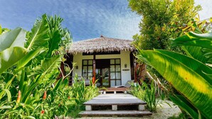 Una cabaña con techo de paja y terraza de madera, rodeada de exuberante vegetación tropical.