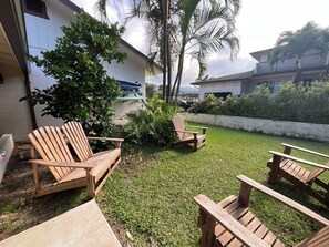 Eine Terrasse mit Holzstühlen, einem kleinen Baum und einem weißen Gebäude im Hintergrund.