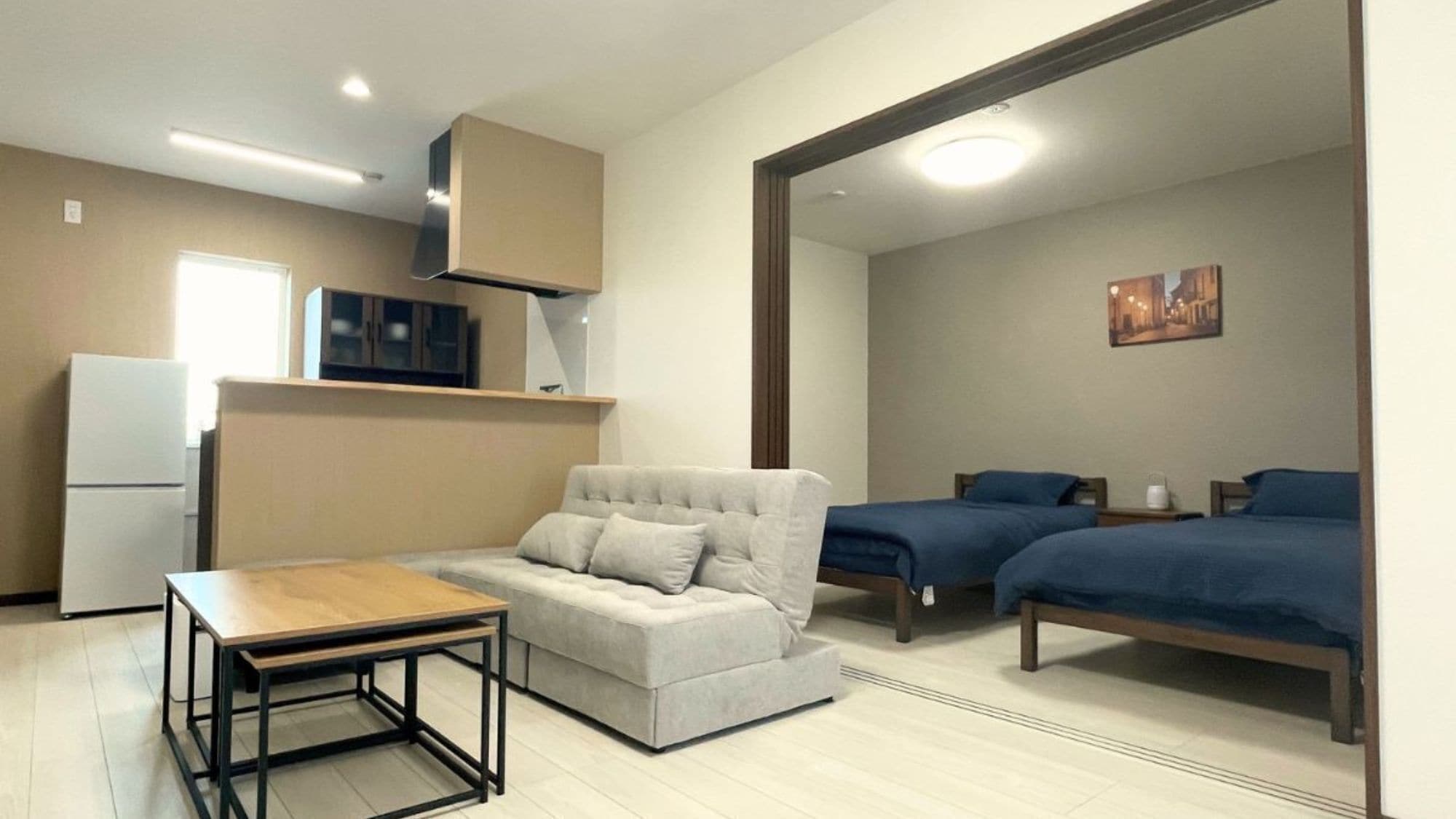 A compact room with a kitchenette, a sofa, two single beds, and a small table.