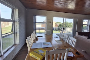 A spacious room with a long wooden table, white chairs, and large windows offering a view of the outdoors. - Spacious Family Holiday Home - Entire House Rental (Franskraal)