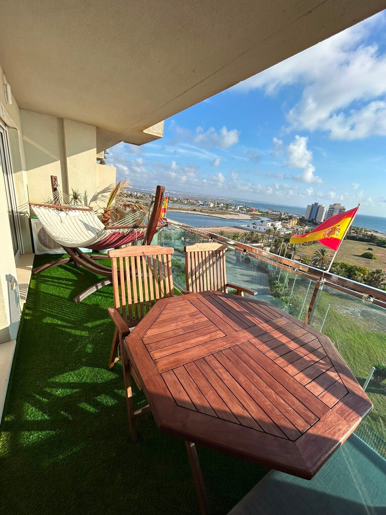 Un balcon avec une table et des chaises en bois, un hamac et un drapeau.