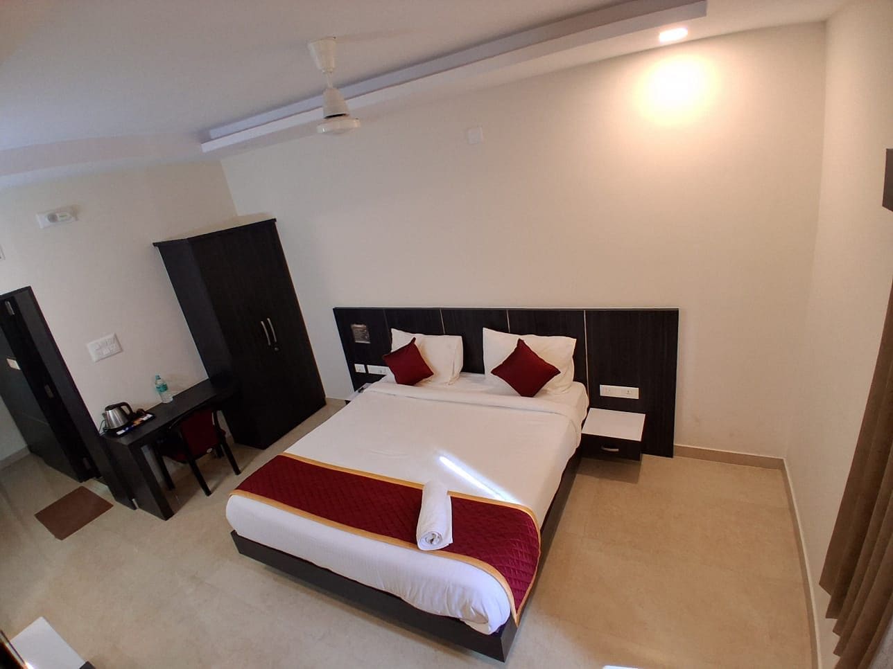 Quarto de hotel com cama, escrivaninha, armário e ventilador de teto.