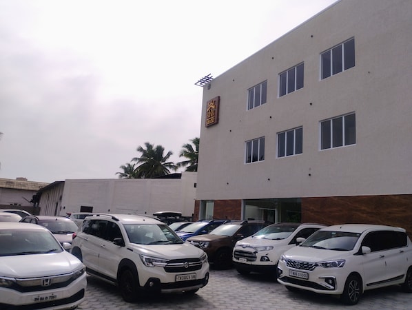 A parking lot with multiple vehicles, a building with a sign, and palm trees in the background.