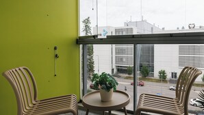 A room with a green wall, two wicker chairs, a round table with a potted plant, and a view of buildings through a large window.
