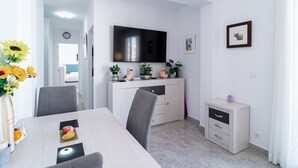 A modern dining area with a flat-screen TV, a white cabinet with decorative items, and a small bedside table. - Chaparil Seaview by Casasol (Nerja)