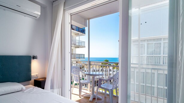 A hotel room with a bed, a bedside table, a nightstand, a balcony with a table and chairs, and a view of the sea. - Chaparil Seaview by Casasol (Nerja)