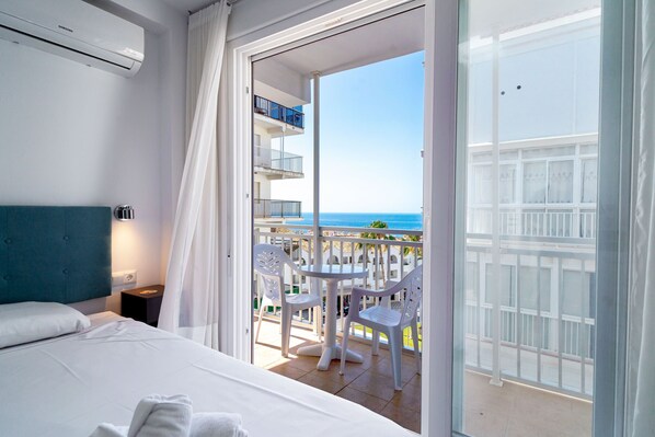 Ein Hotelzimmer mit Bett, Nachttisch, Tisch mit Stühlen und einem Balkon mit Meerblick.