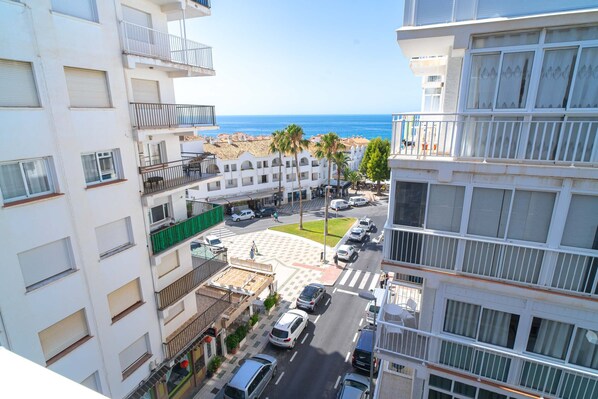 Un immeuble à plusieurs étages doté de balcons, une rue bordée de voitures et une vue sur la mer.