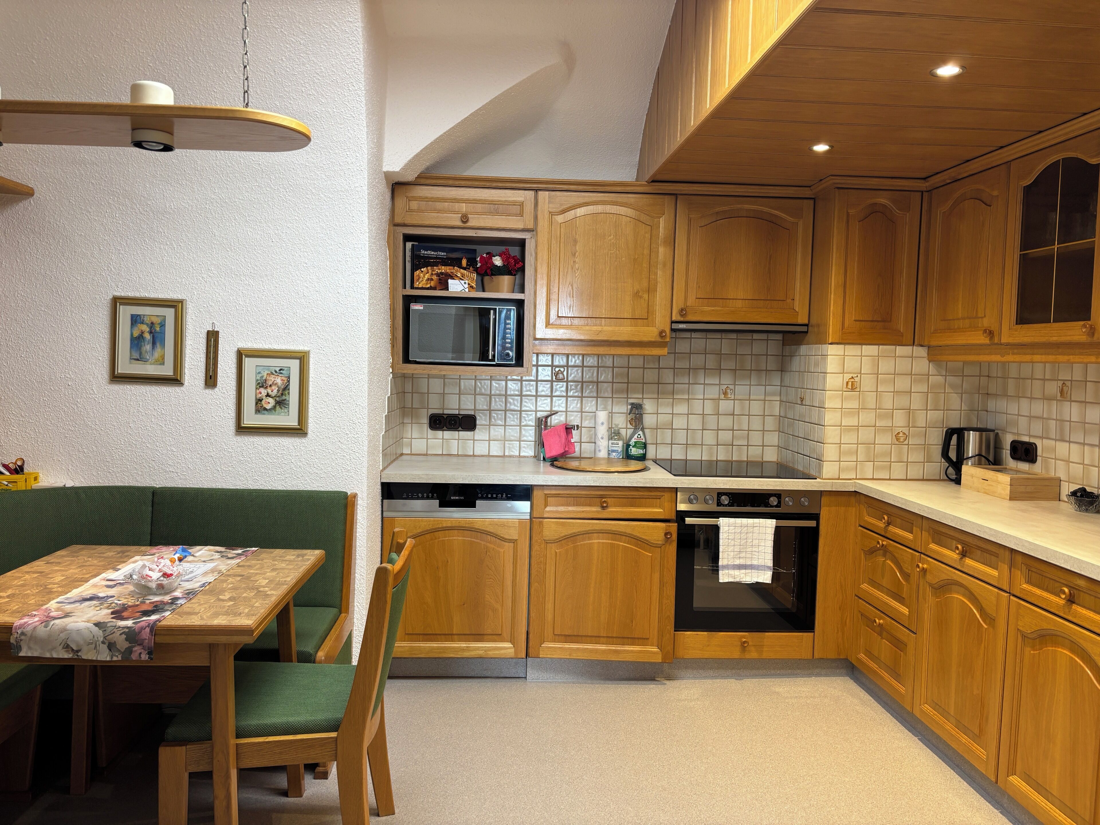 Een keuken met houten kastjes, een magnetron, een fornuis en een eethoek met een tafel en stoelen.