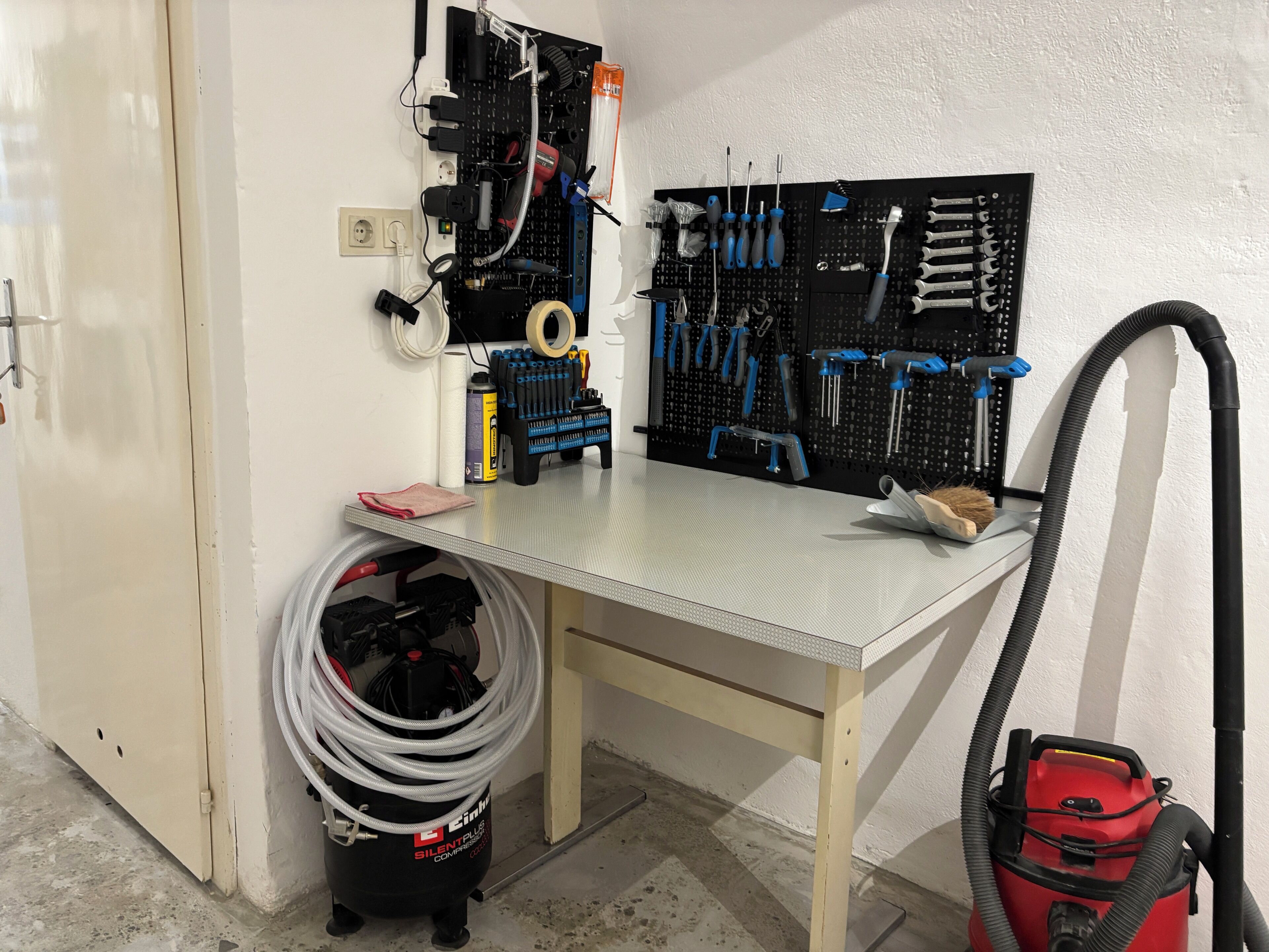 A workshop with a pegboard wall, a workbench, and various tools.
