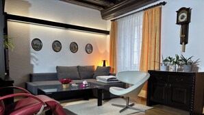 En moderne stue med sofa, sofabord i glas, rød lænestol og et mørkt træskab.