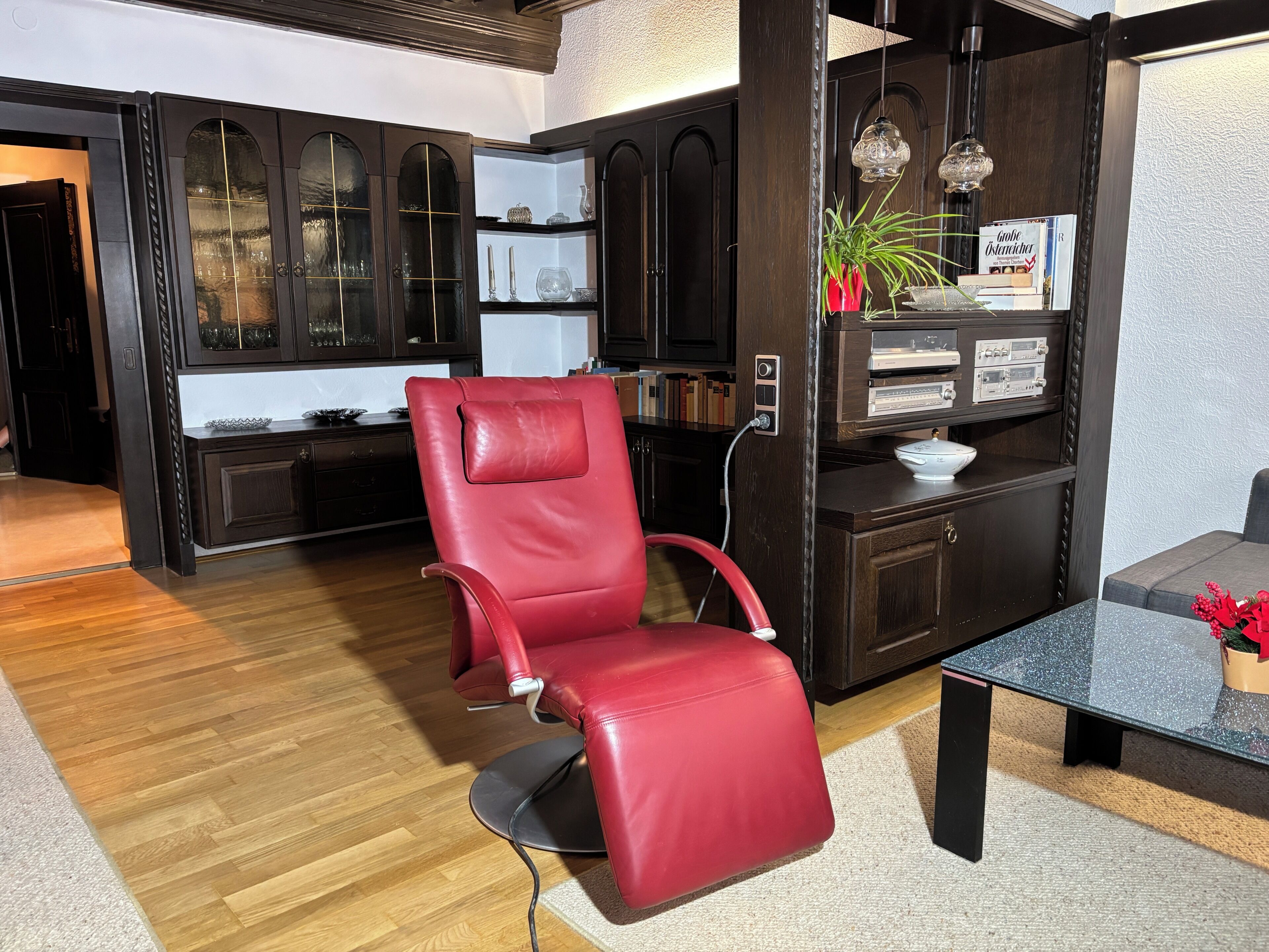 A modern living room with a red leather chair, dark wooden cabinets, and a glass coffee table.