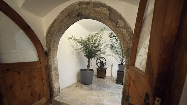 En stenbuet indgang til en lille gårdsplads med en potteplante og en metal skulptur.