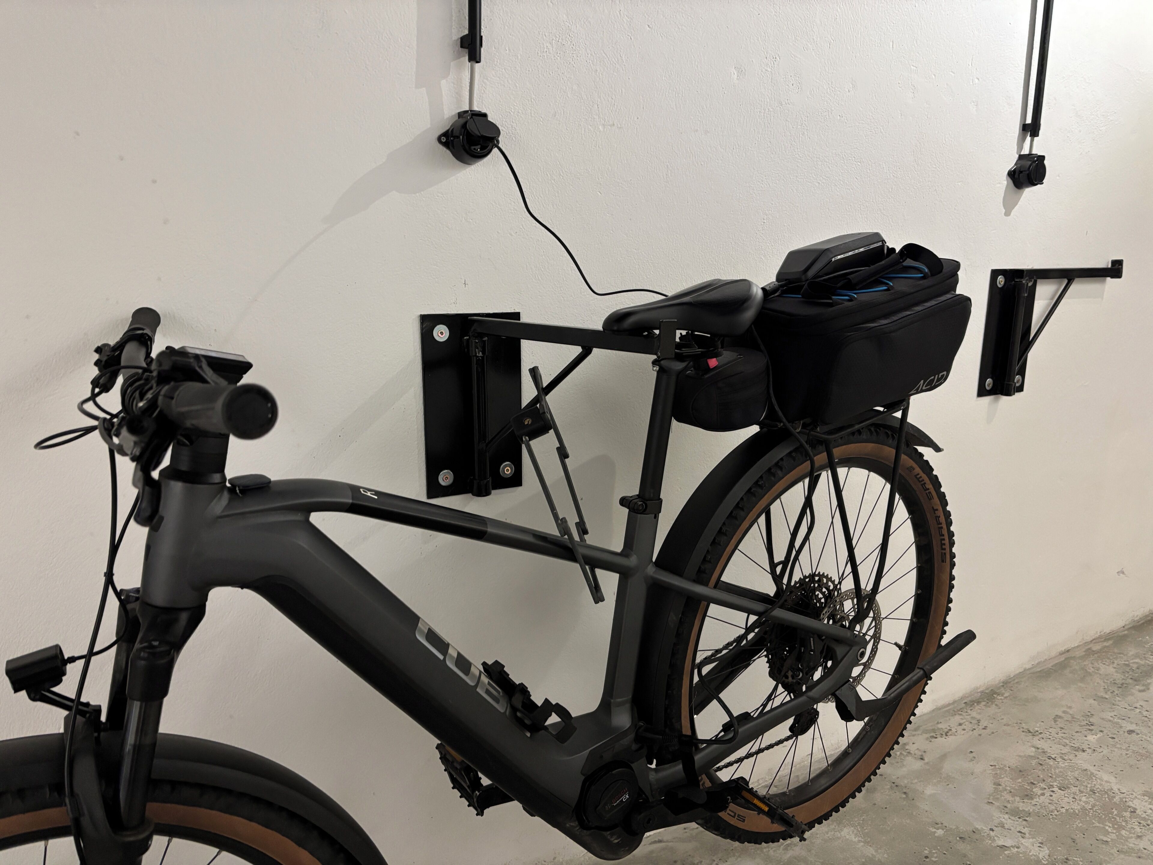 A stationary bicycle with a front-mounted device, a rear rack, and a black bag attached to the rear.