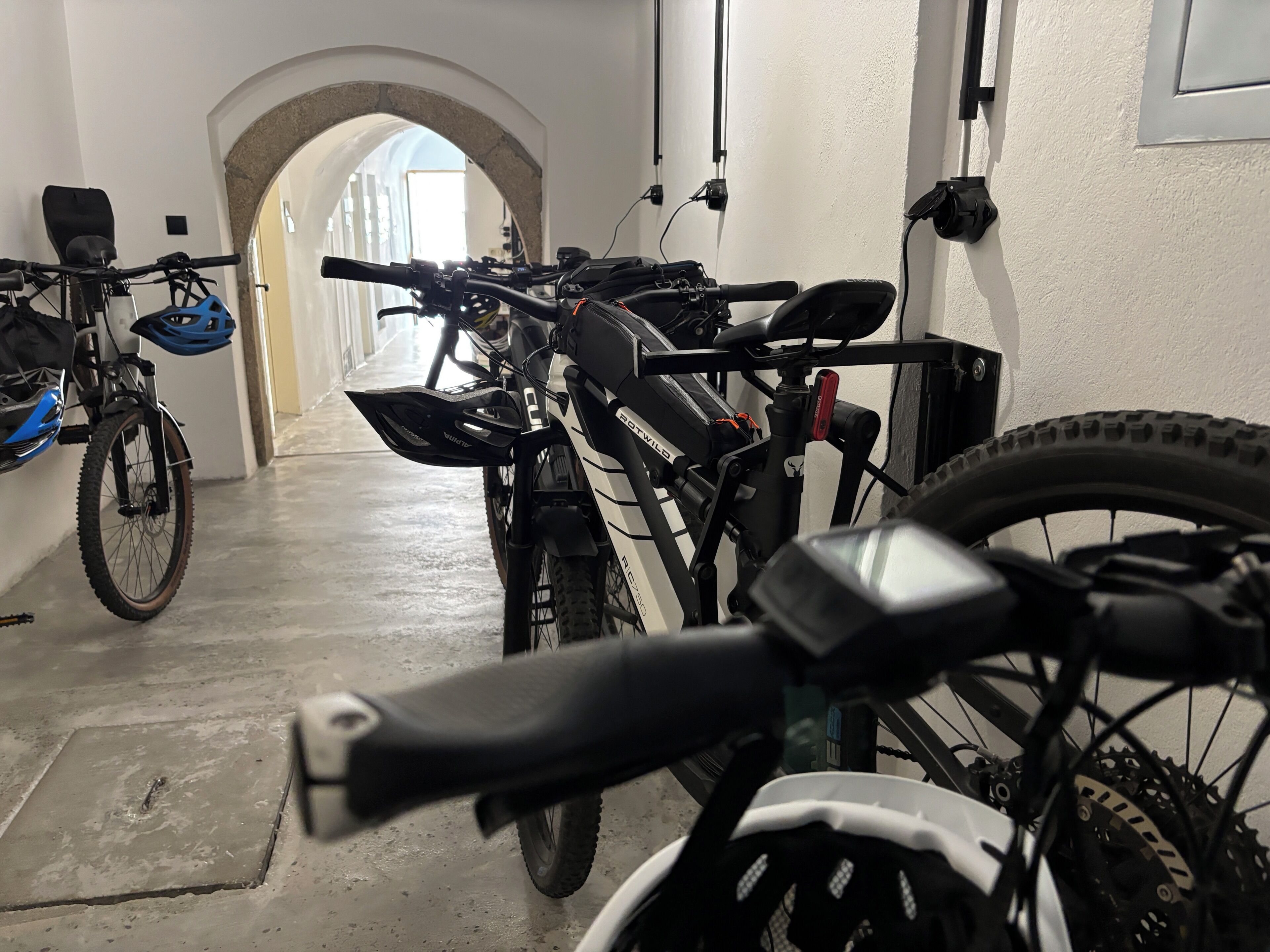 A bicycle storage area with multiple bikes, a concrete floor, and an arched doorway leading to another room.