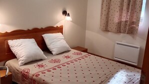 Una camera da letto con un letto, un comodino, una lampada a parete, una finestra con tende e un termosifone.