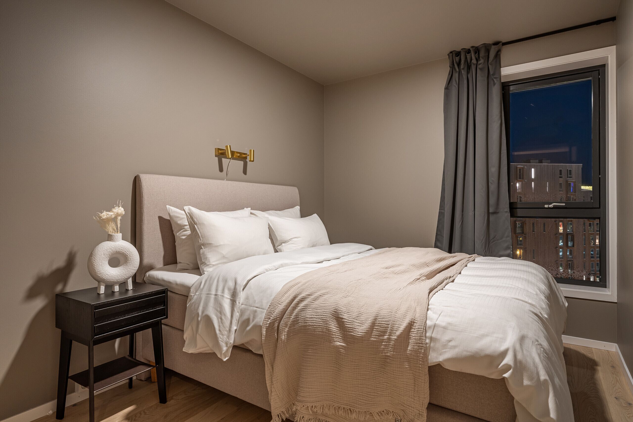 A bedroom with a bed, bedside table, and a window with curtains.