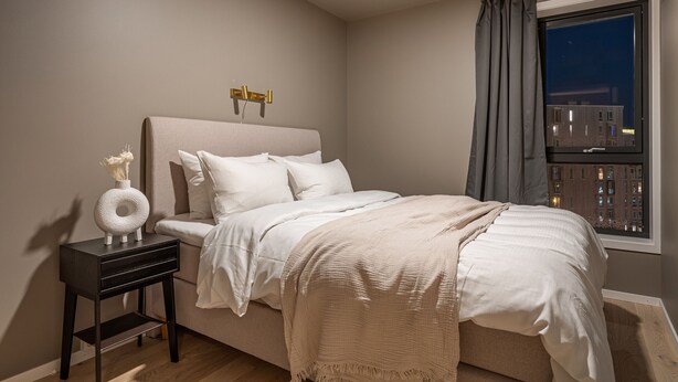 Un dormitorio con cama, mesita de noche y ventana con cortinas.