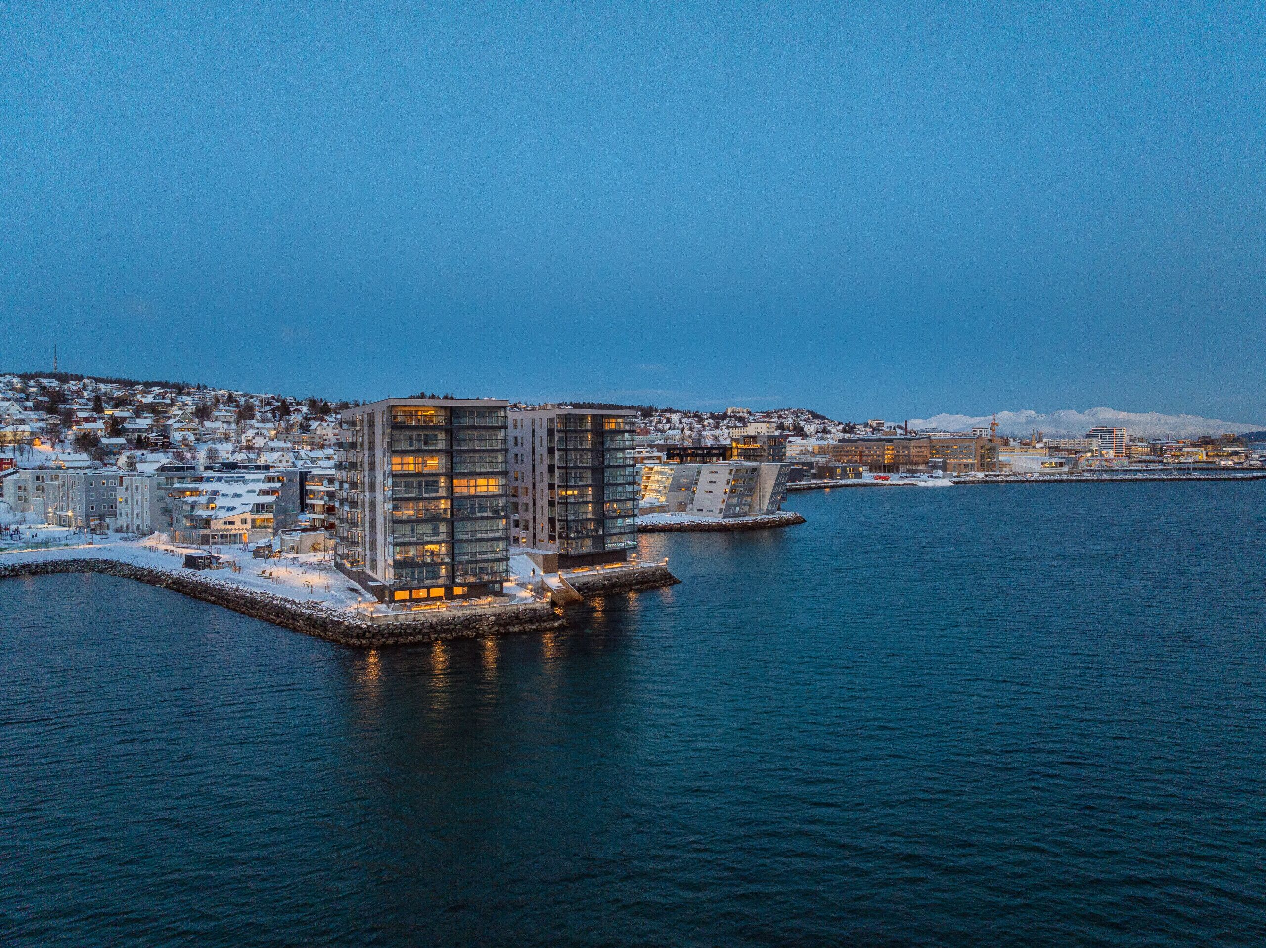 A waterfront hotel with modern architecture, a dock, and a view of the cityscape.