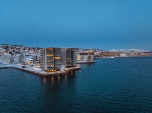 Ein Hotel am Wasserufer, mit moderner Architektur, einem Steg und Blick auf die Skyline der Stadt.