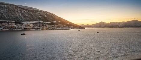 A coastal town with a calm sea, boats, and snow-covered mountains.