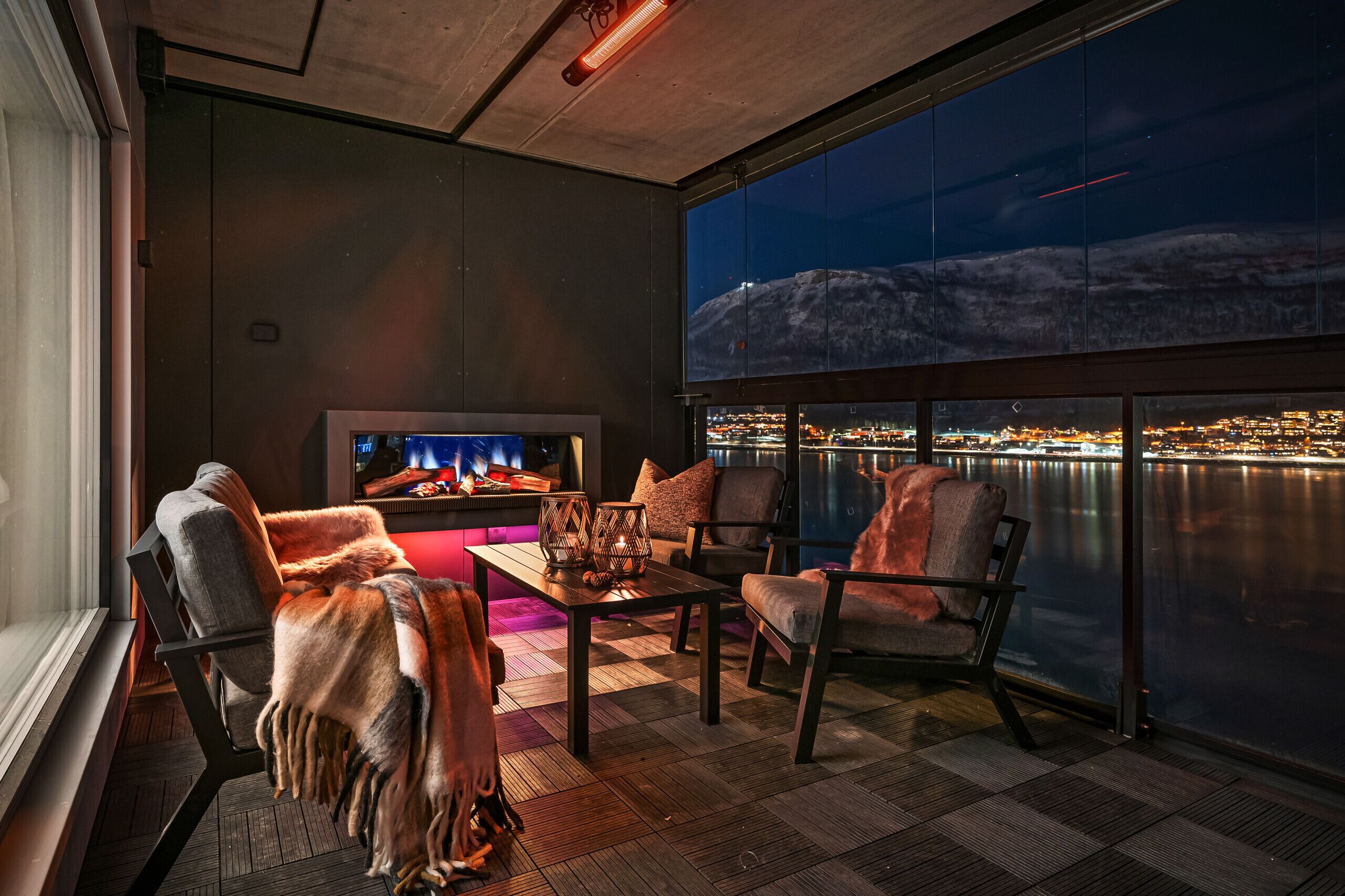 A modern lounge with a fireplace, comfortable seating, and a large window overlooking a cityscape at night.