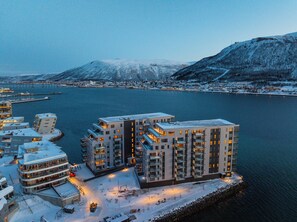 A modern hotel with multiple floors, a waterfront location, and a view of a snowy mountain range. - Eight floor Premium Waterfront Penthouse (Tromsø)