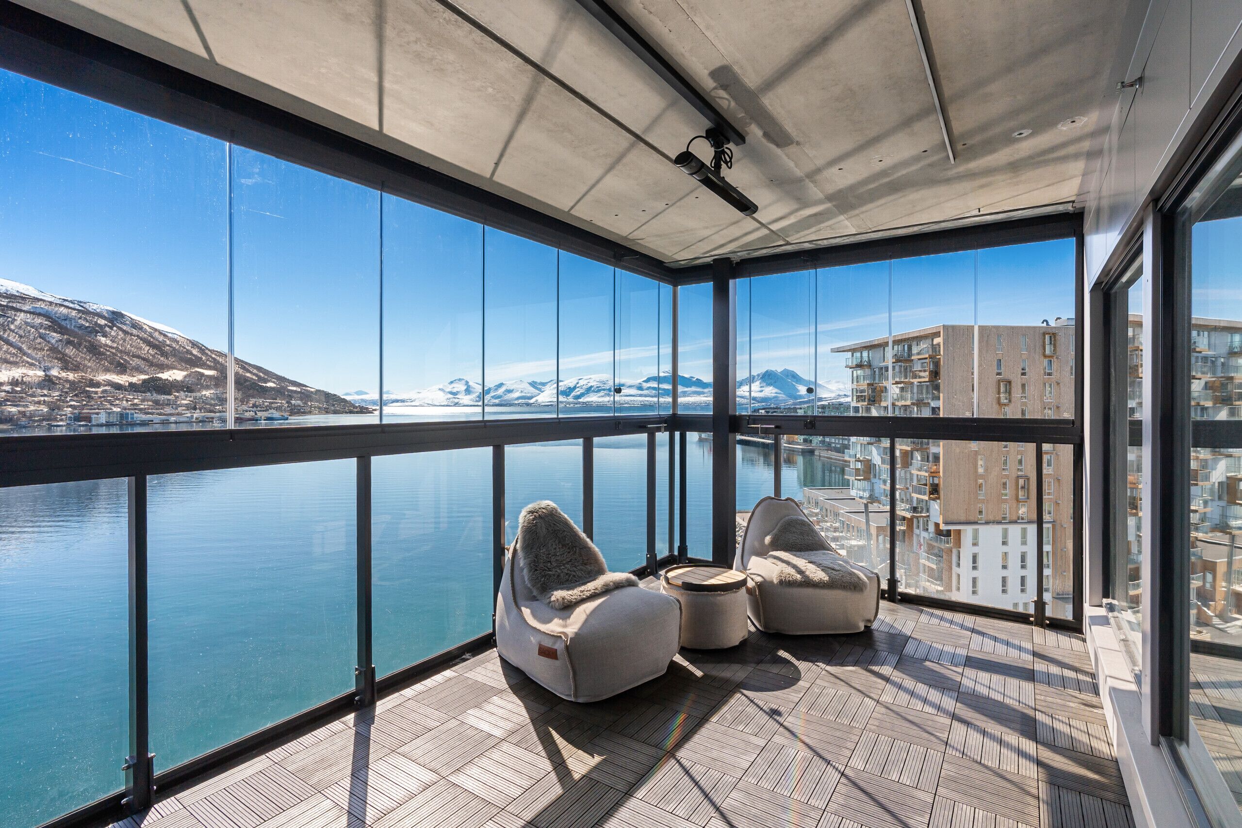 Een balkon met uitzicht op een waterpartij en bergen, voorzien van twee kruiskladers en een kleine tafel.